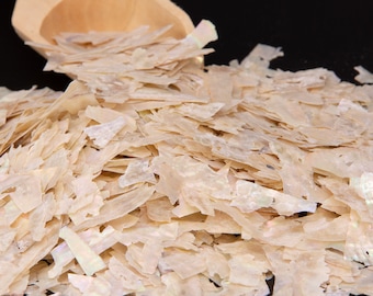 May include: A pile of iridescent white and beige mother of pearl shell flakes. The flakes are various sizes and shapes.