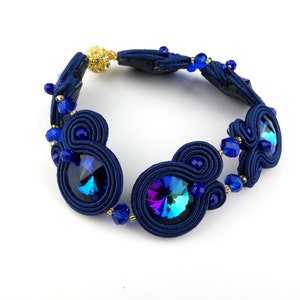 Peut inclure: Un bracelet bleu marine avec deux gros cristaux bleus iris&eacute;s et de petites perles bleues. Le bracelet est fait d'un cordon tress&eacute; et a un fermoir dor&eacute;.