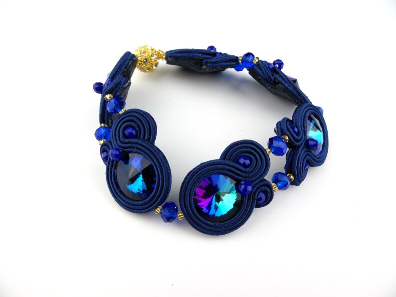 Peut inclure: Un bracelet bleu marine avec deux gros cristaux bleus iris&eacute;s et de petites perles bleues. Le bracelet est fait d'un cordon tress&eacute; et a un fermoir dor&eacute;.