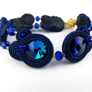 Peut inclure: Un bracelet bleu marine avec des perles bleues et dor&eacute;es et un grand cristal bleu. Le bracelet est fait de cordon tress&eacute; et a un design unique et complexe.