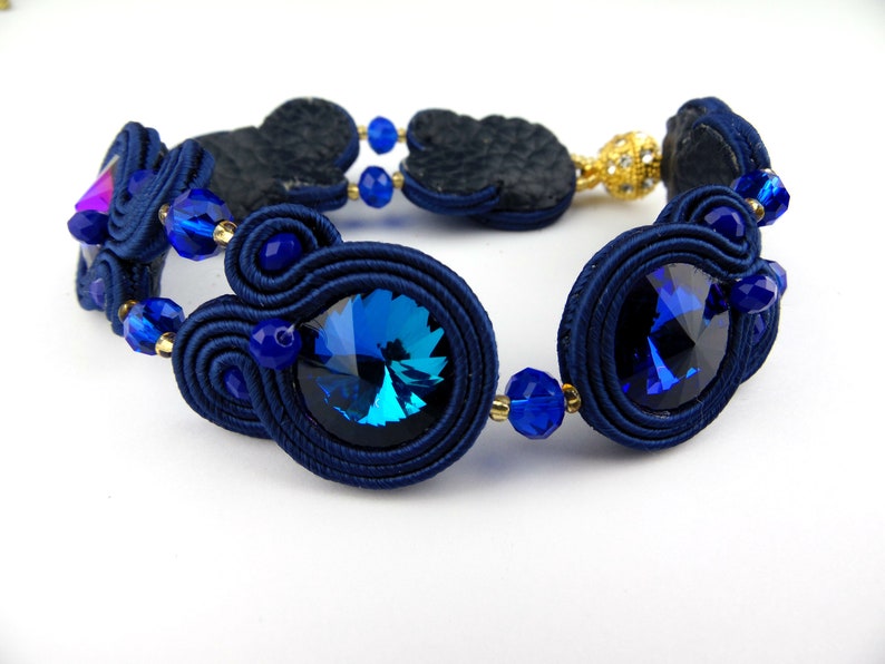 Peut inclure: Un bracelet bleu marine avec des perles bleues et dor&eacute;es et un grand cristal bleu. Le bracelet est fait de cordon tress&eacute; et a un design unique et complexe.