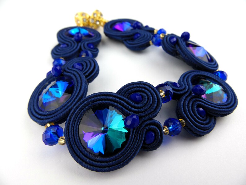 Peut inclure: Un bracelet bleu marine avec des cristaux bleus iris&eacute;s et des accents dor&eacute;s. Le bracelet est fait de cordon tress&eacute; et pr&eacute;sente un design unique et complexe.