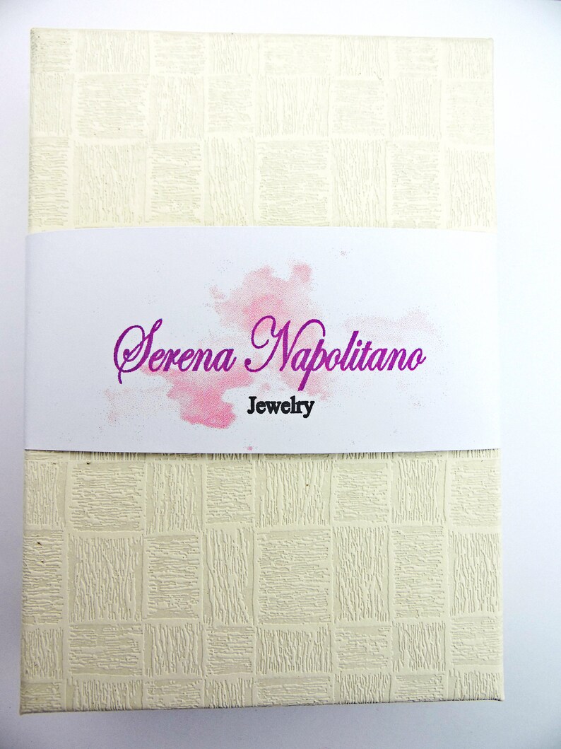 Peut inclure: Une bo&icirc;te blanche avec une surface textur&eacute;e et un motif aquarelle rose. Le texte "Serena Napolitano Jewelry" est imprim&eacute; en violet sur la bo&icirc;te.