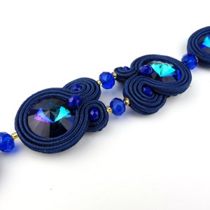 Peut inclure: Un collier en cristal bleu et iridescent avec un design de cordon tiss&eacute;. Le collier pr&eacute;sente plusieurs perles de cristal et un design de cordon tiss&eacute;.