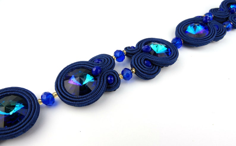 Peut inclure: Un collier en cristal bleu et iridescent avec un design de cordon tiss&eacute;. Le collier pr&eacute;sente plusieurs perles de cristal et un design de cordon tiss&eacute;.