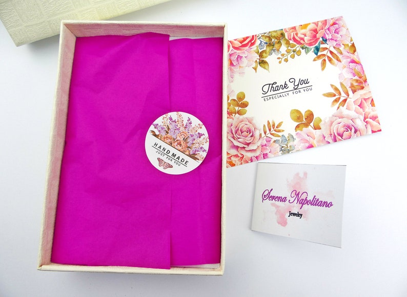 May include: A white gift box with a pink tissue paper lining. The box has a sticker that says "Hand Made Just For You". The box is next to a thank you card with a floral design and the text "Thank You Especially For You". There is also a business card that says "Serena Napolitano Jewelry".