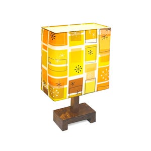 May include: A mid-century modern table lamp with a rectangular shade. The shade features a pattern of yellow, orange, and brown rectangles and starbursts. The base is a dark brown, rectangular block. The lamp is a decorative lighting fixture.