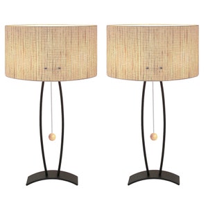 May include: Two matching table lamps with oval, woven shades. The lamps have a dark bronze finish with a curved base and stem. Each lamp has a pull chain with a wooden ball. The shades are beige and tan.