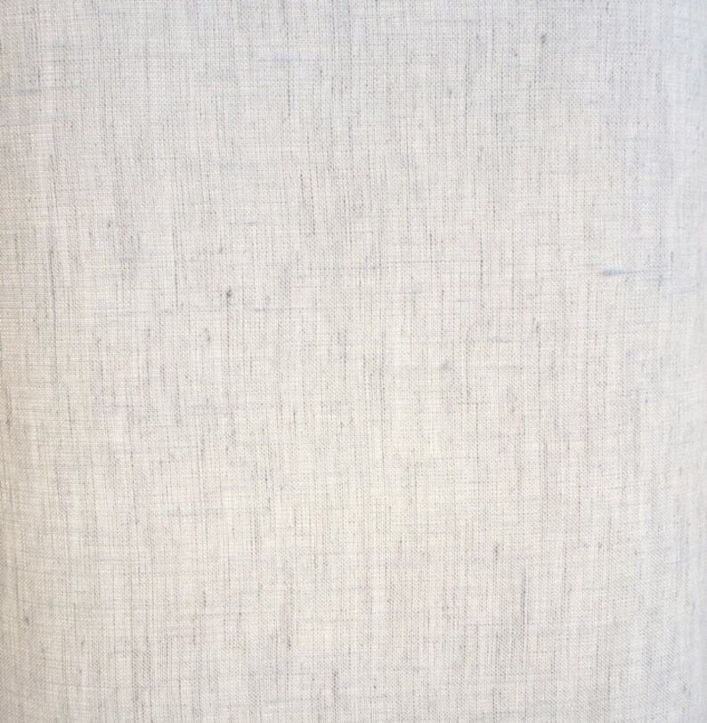 May include: Close-up of a light gray linen fabric. The texture is visible, showing the weave of the threads. The fabric appears to be a natural material, possibly used for clothing or home decor.