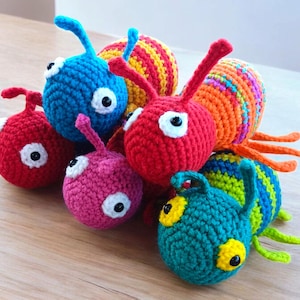 May include: A group of six crocheted colorful toy bugs. The bugs are red, orange, yellow, green, blue, and pink. They have large, white eyes and are made with a variety of stitches.