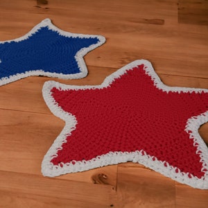May include: Two crocheted star-shaped rugs, one blue and one red, with white trim. The rugs are on a wooden floor.
