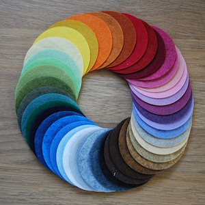 May include: A rainbow of felt circles arranged in a circle, with the colours transitioning from orange to red, pink, purple, blue, green, and yellow.