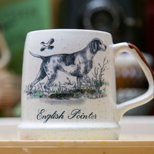 May include: White ceramic mug with a brown handle. The mug features a black and white illustration of an English Pointer dog and a bird in flight. The text "English Pointer" is printed on the mug.