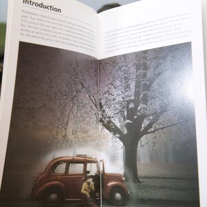 Op de afbeelding: Open boek met de titel "Introduction" zichtbaar. De pagina's tonen een foto van een vintage rode auto met een persoon, tegen een achtergrond van een besneeuwde boom en een mistig bos. De tekst op de pagina is gedeeltelijk zichtbaar.