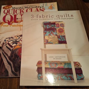 May include: Two quilting books are displayed. The book on the left is titled "New Quick Quilts" by Marsha McCloskey. The book on the right is titled "3-fabric quilts" with a small quilt displayed on a miniature white chair.