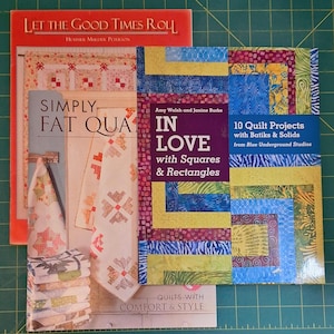 May include: A stack of quilting books with colorful covers. Titles include "Let the Good Times Roll," "Simply Fat Quas," and "In Love with Squares & Rectangles." The books feature quilt patterns and designs, perfect for sewing enthusiasts.