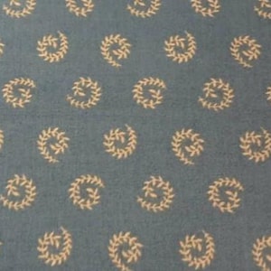 May include: A close-up of a blue fabric with a repeating pattern of cream-colored, stylized leaf spirals. The spirals are evenly spaced across the fabric, creating a textured appearance. The fabric has a slightly faded look.