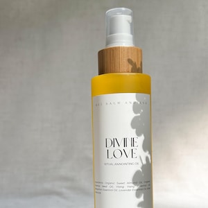 以下が含まれることがあります： 白いラベルと木製のキャップが付いた、黄色のガラス瓶に入った「DIVINE LOVE」儀式用アノインティングオイル。ラベルには成分とブランド名「BEE BALM AND ASH」が記載されています。ボトルには118mlが入っています。