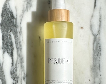 May include: A clear glass bottle of perineal massage oil with a wooden cap and white label. The label reads "PERINEAL MASSAGE OIL" and lists ingredients. The bottle contains a yellow liquid and is 4 oz in size.