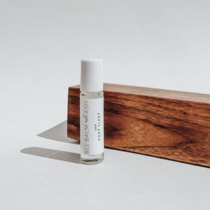 Könnte beinhalten: Eine weiße Rollflasche mit einem Etikett, auf dem "BEE BALM + ASH" und "adult DEEP SLEEP" steht. Die Flasche steht auf einer Holzoberfläche.