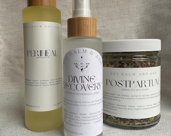 May include: Three Bee Balm and Ash postpartum care products: a massage oil, a perineal spray, and a herbal sitz bath blend. The bottles have wooden caps and white labels with black text. The massage oil is in a clear bottle with a yellow liquid.