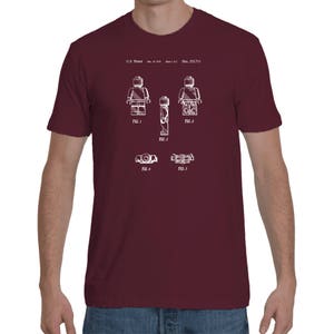 May include: A maroon t-shirt with a white print of a Lego figure patent design. The design includes five figures and the text "U.S. Patent Des. 253,711".