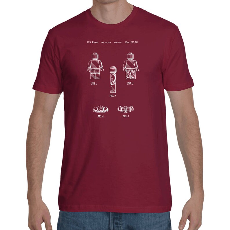 May include: A maroon t-shirt with a white print of a Lego figure patent design. The patent number is U.S. Patent: Dec. 18, 1979, Des. 253,711.