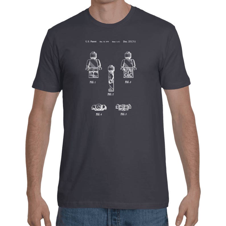 May include: A dark gray t-shirt with a white print of a Lego figure patent drawing. The drawing shows the figure in different positions and includes the text "U.S. Patent: Dec. 23, 1977", "FIG. 1", "FIG. 2", "FIG. 3", "FIG. 4", and "FIG. 5".