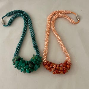 May include: Two beaded necklaces. One is teal with green stone accents, the other is peach with red stone accents. Both have magnetic clasps. The necklaces are displayed on a white surface.