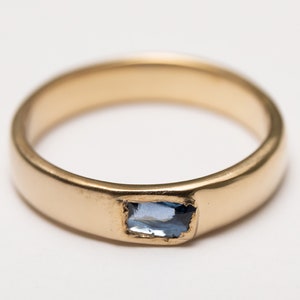 May include: A gold band ring with a light blue rectangular gemstone set in the centre.