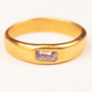 Puede incluir: Un anillo de banda de oro con una piedra rectangular de color púrpura claro engastada en el centro.