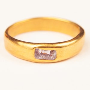 May include: A gold band ring with a rectangular, light purple gemstone set in the centre.