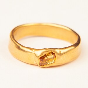 May include: A gold ring with a textured band and a small, rectangular, orange gemstone.