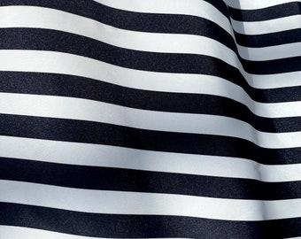 May include: Black and white striped fabric with a smooth, shiny texture. The fabric is folded and draped, creating a wave-like pattern.