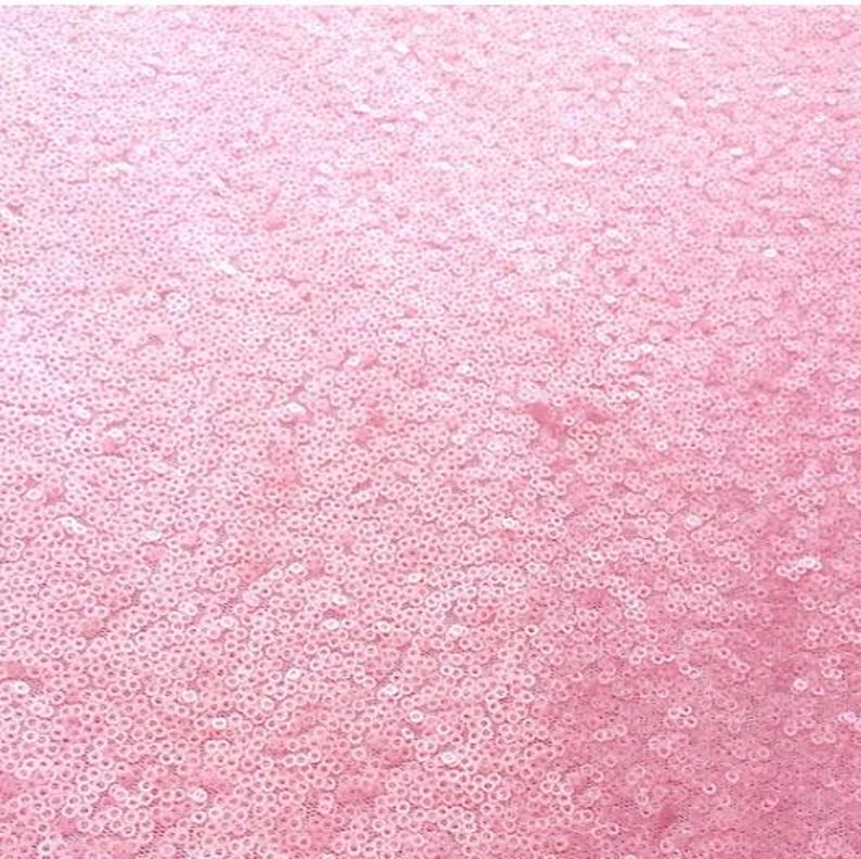 Puede incluir: Primer plano de una tela de lentejuelas rosas. Las lentejuelas, peque&ntilde;as y redondas, est&aacute;n densamente dispuestas, creando una superficie texturizada y brillante. El color es un rosa suave y claro, con ligeras variaciones de tono. El efecto general es de brillo y glamour.