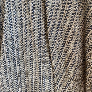 May include: Close-up of a woven fabric with a black and beige pattern. The fabric has a textured surface and a herringbone design.