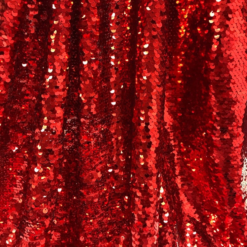 Puede incluir: Primer plano de una vibrante tela de lentejuelas rojas. Las lentejuelas est&aacute;n densamente empaquetadas, creando una superficie brillante y texturizada. La tela est&aacute; drapeada, con pliegues y sombras que a&ntilde;aden profundidad y dimensi&oacute;n. Las lentejuelas reflejan la luz.