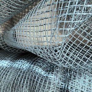 May include: Close-up of a gray, woven mesh fabric with a grid pattern. The fabric is folded and draped, creating a textured and abstract look.