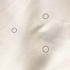 May include: Close-up of a white fabric with three small, circular holes.