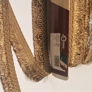 May include: A roll of gold acetate fringe trim with a label that reads "Conso 009115 E16 Acetate Fringe 2 1/4" (2.25) 300 yd.  Coll. 200"