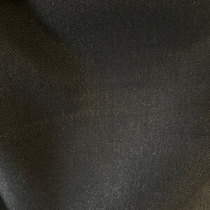 Pode incluir: Tecido preto com trama texturizada. O tecido tem um brilho sutil.