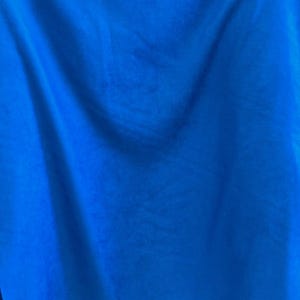 May include: A vibrant royal blue fabric with a smooth, matte texture. The material is draped in soft, flowing folds, creating subtle variations in light and shadow across the surface. The textile appears opaque and consistent in its deep blue color.