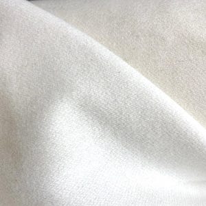 Puede incluir: Primer plano de una tela blanca rota doblada. El material tiene un aspecto suave y texturizado con sutiles variaciones de tono. Los pliegues crean sombras y reflejos, añadiendo profundidad a la imagen. La tela parece ser de peso medio.