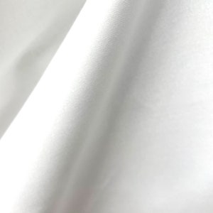 Puede incluir: Tela blanca con una textura lisa y un ligero brillo. La tela está doblada de forma que crea una línea diagonal.