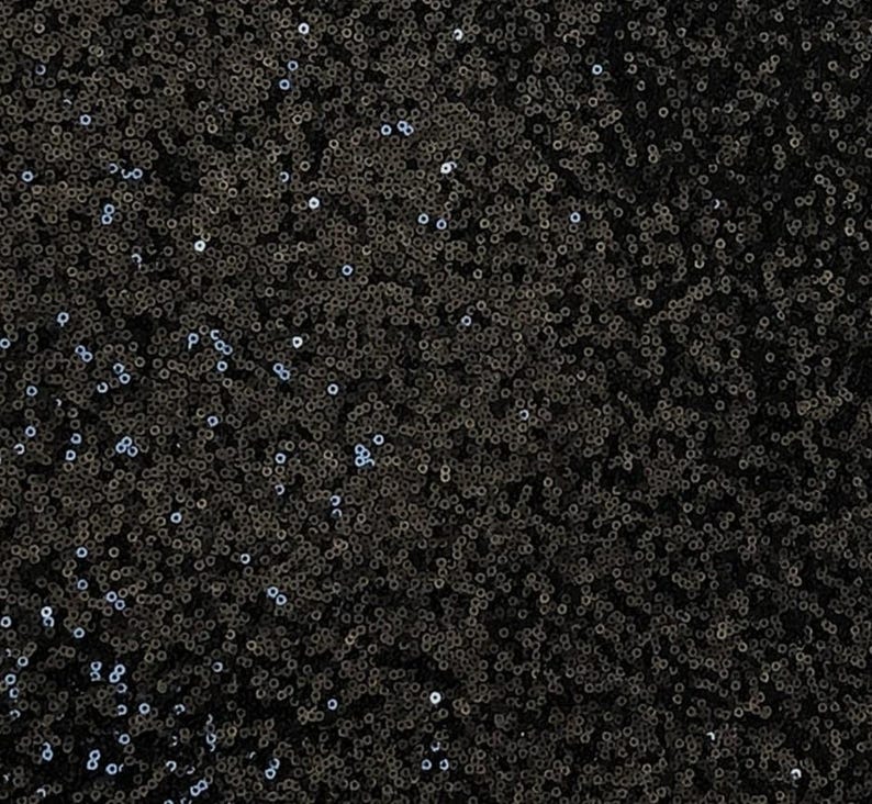 Puede incluir: Primer plano de una tela de lentejuelas negras. Las lentejuelas, peque&ntilde;as y redondas, est&aacute;n densamente dispuestas, creando una superficie texturizada y brillante. La tela refleja la luz, con sutiles variaciones tonales.