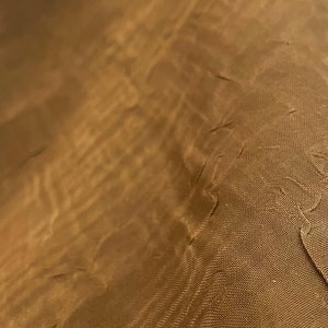 May include: Close-up of a brown fabric with a textured, woven pattern. The fabric has a subtle sheen and a slightly wrinkled appearance.