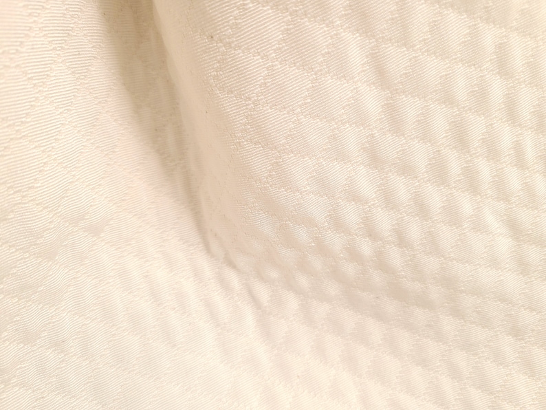 May include: Close-up of a white fabric with a subtle diamond pattern. The fabric has a soft, smooth texture.