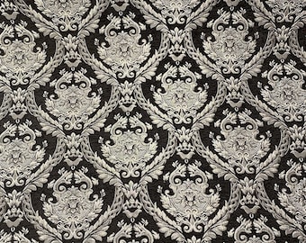 May include: Close-up of a black and silver damask fabric. The pattern features a repeating design of ornate floral and scroll motifs in a metallic silver color against a dark background. The fabric has a textured appearance.