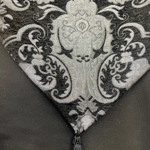 May include: A black and silver table runner with a damask pattern and a black tassel.