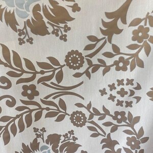May include: Close-up of a fabric with a repeating floral pattern. The design features brown floral elements and leaves on a white background. Some light blue floral accents are also visible.